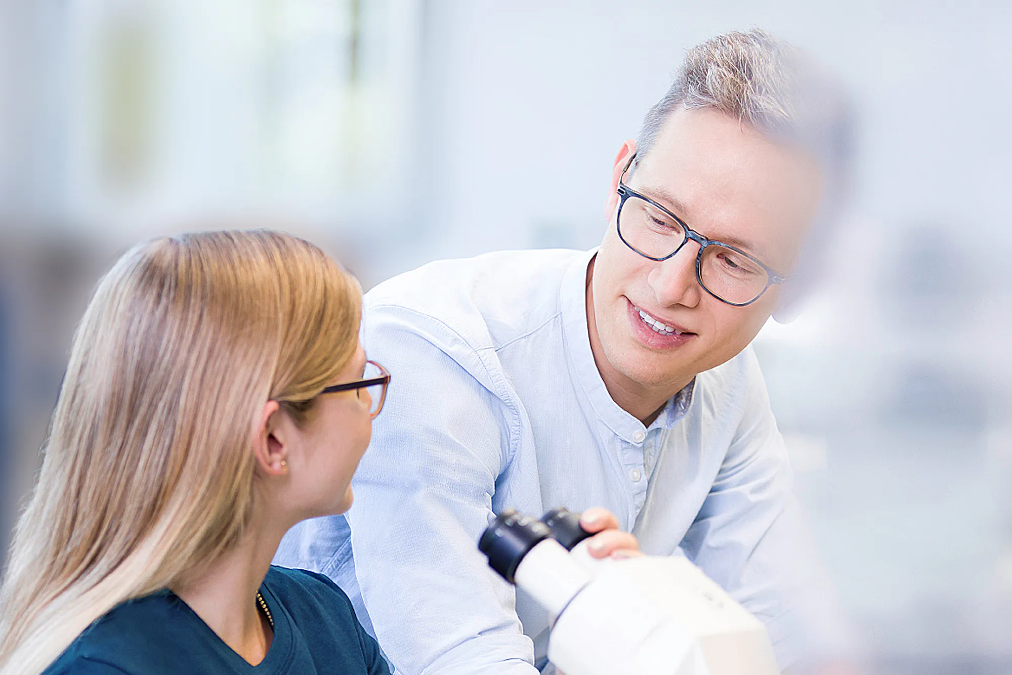 Mitarbeiterfotografie von zwei jungen Mitarbeitern im Gespräch an einem Arbeitsplatz mit mikroskop.